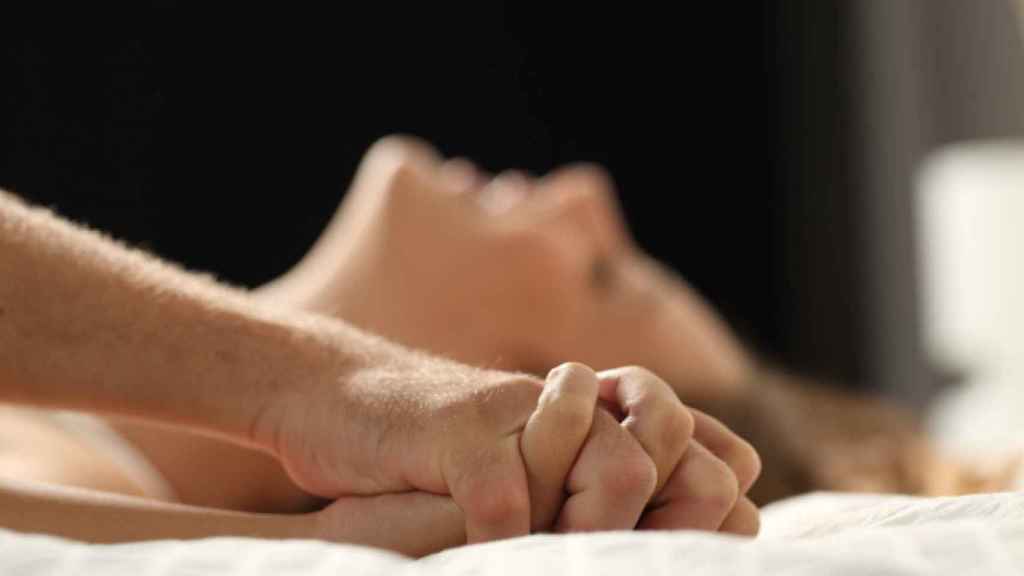 Una pareja mantiene relaciones sexuales con las manos entrelazadas.