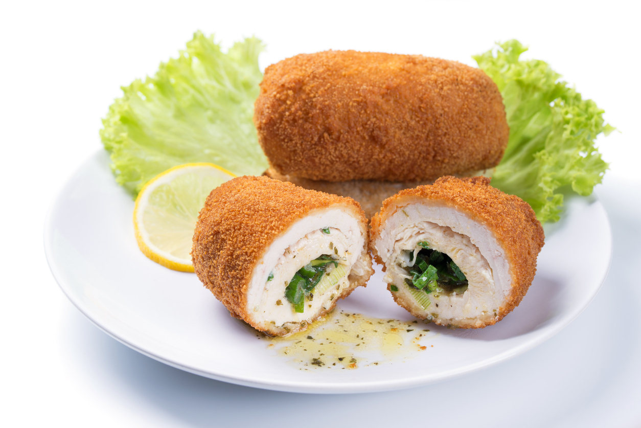 Chicken Kiev cutlet with green salad and lemon slice on a plate, white background
